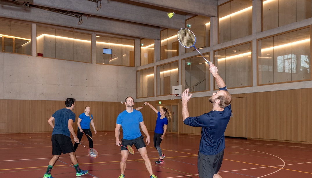 Männer und Frauen spielen Badminton in einer Turnhalle