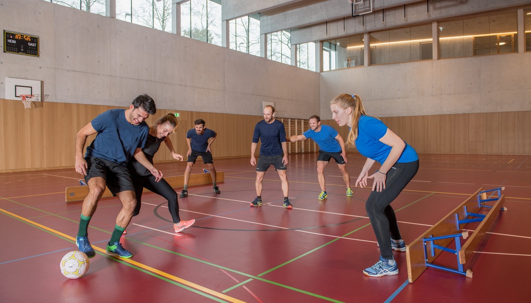 Frauen und Männer spielen Bänklifussball in einer Turnhalle