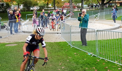 Radrennen in einem im Freibad Weyermannshaus, eine Frau fährt auf einem Fahrrad, während Zuschauer und weitere Radfahrende im Hintergrund stehen.