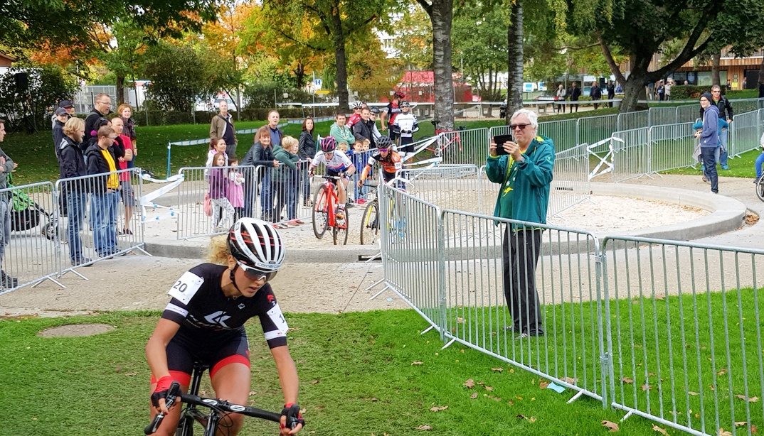 Radrennen in einem im Freibad Weyermannshaus, eine Frau fährt auf einem Fahrrad, während Zuschauer und weitere Radfahrende im Hintergrund stehen.