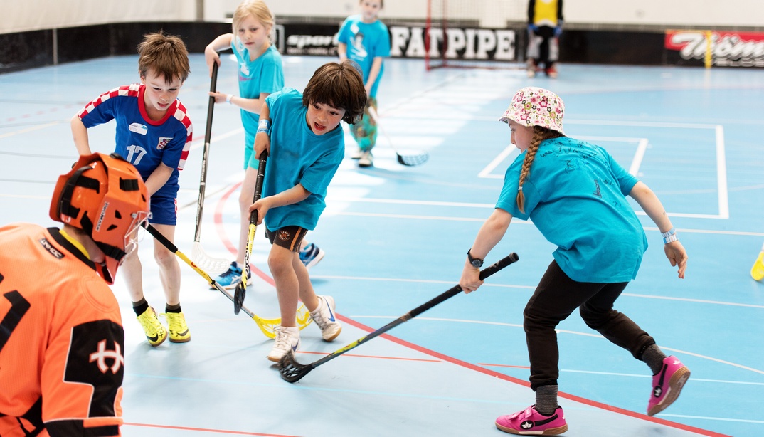 Kinder spielen Unihockey in einer Sporthalle.
