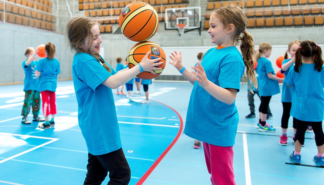 Zwei Mädchen spielen Basketball in einer Turnhalle.