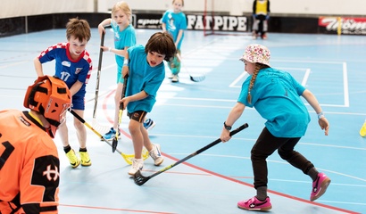 Kinder spielen Unihockey in einer Sporthalle.