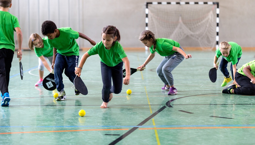 Kinder rennen Tennisbällen hinterher in einer Turnhalle