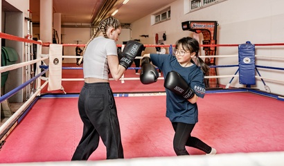 Zwei Mädchen mit Boxhandschuhen trainieren in einem Boxring; eine schlägt, die andere wehrt ab.
