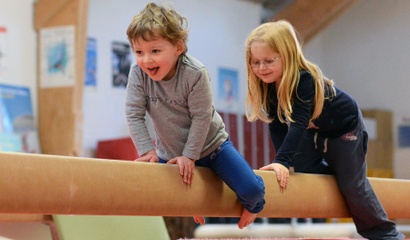 Zwei Kinder balancieren auf einem Turnbalken in einer Turnhalle.