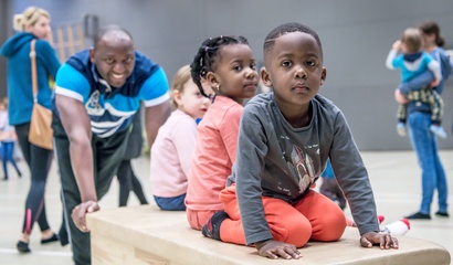 Zwei Kinder sitzen auf einem Schwedenkasten in einer Turnhalle.