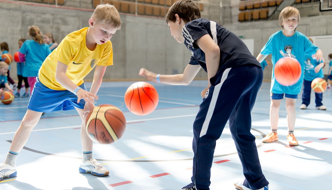 Kinder spielen Basketball in einer Halle.