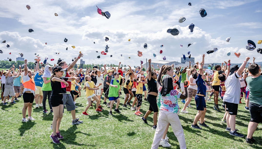 Viele Kinder auf einer Wiese werfen ihre Hüte in die Luft.