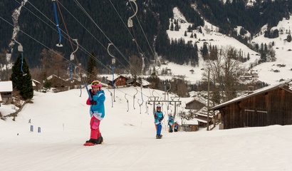 Zwei Kinder fahren mit dem Snowboard an einem Bügellift im Schnee