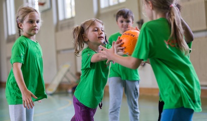 Mädchen in grünen T-Shirts spielen mit einem Basketball in einer Turnhalle