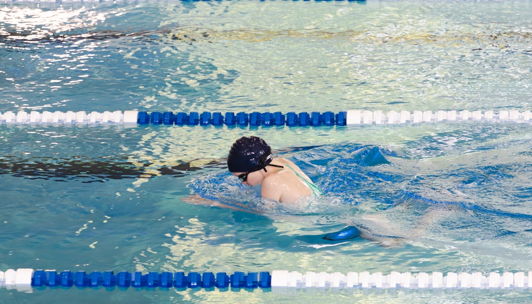 Kind mit Schwimmkappe und Schwimmbrille schwimmt auf einer Schwimmbahn in einem Hallenbad