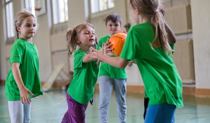Mädchen in grünen T-Shirts spielen mit einem Basketball in einer Turnhalle