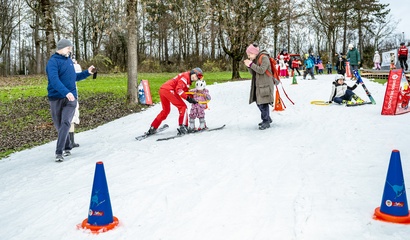Eine Skilehrerin und ein Kind auf Skiern fahren auf der Skipiste im Weyermannshaus, darum herum Erwachsene und andere Kinder