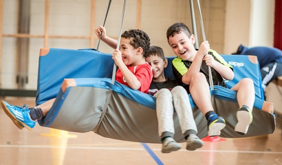 Drei Jungen spielen auf einer Matte an Seilen in einer Turnhalle