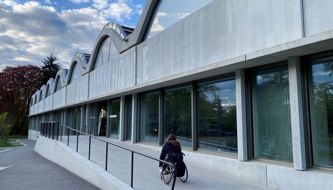 Eine Frau im Rollstuhl fährt die Rollstuhlrampe der Schwimmhalle Neufeld hinauf