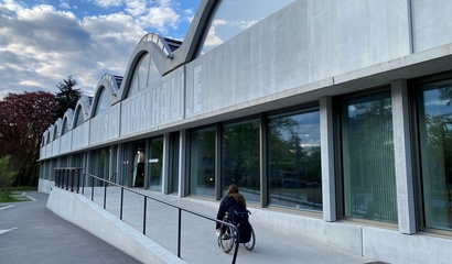 Frau fährt mit Rollstuhl die Rollstuhlrampe der Schwimmhalle Neufeld hinauf